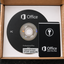 An open cardboard box containing an Office 2021 Professional Plus license card and a branded black disc, photographed from above on a dark textured surface.